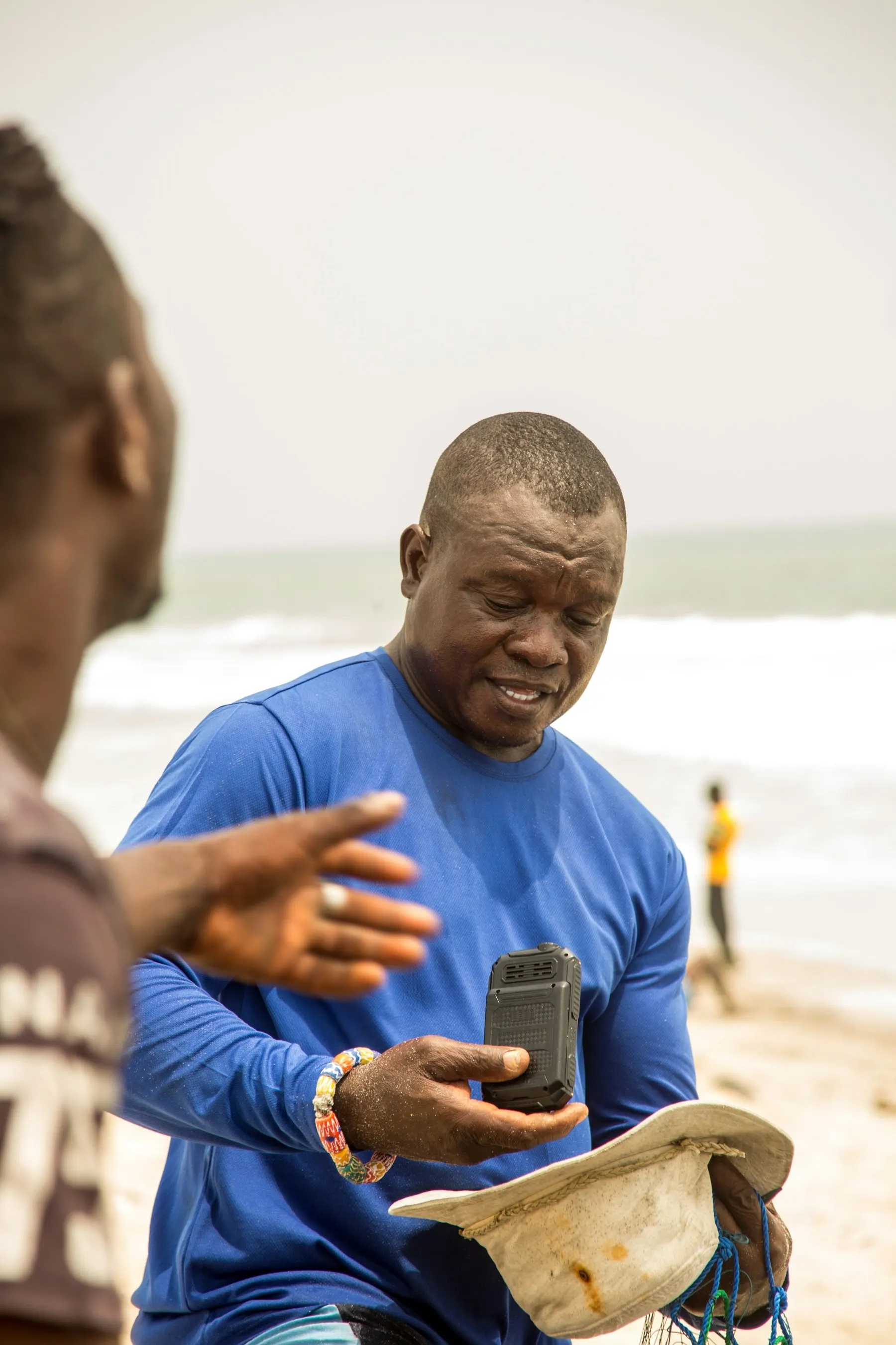 A man in a blue shirt checking a phone on a beach