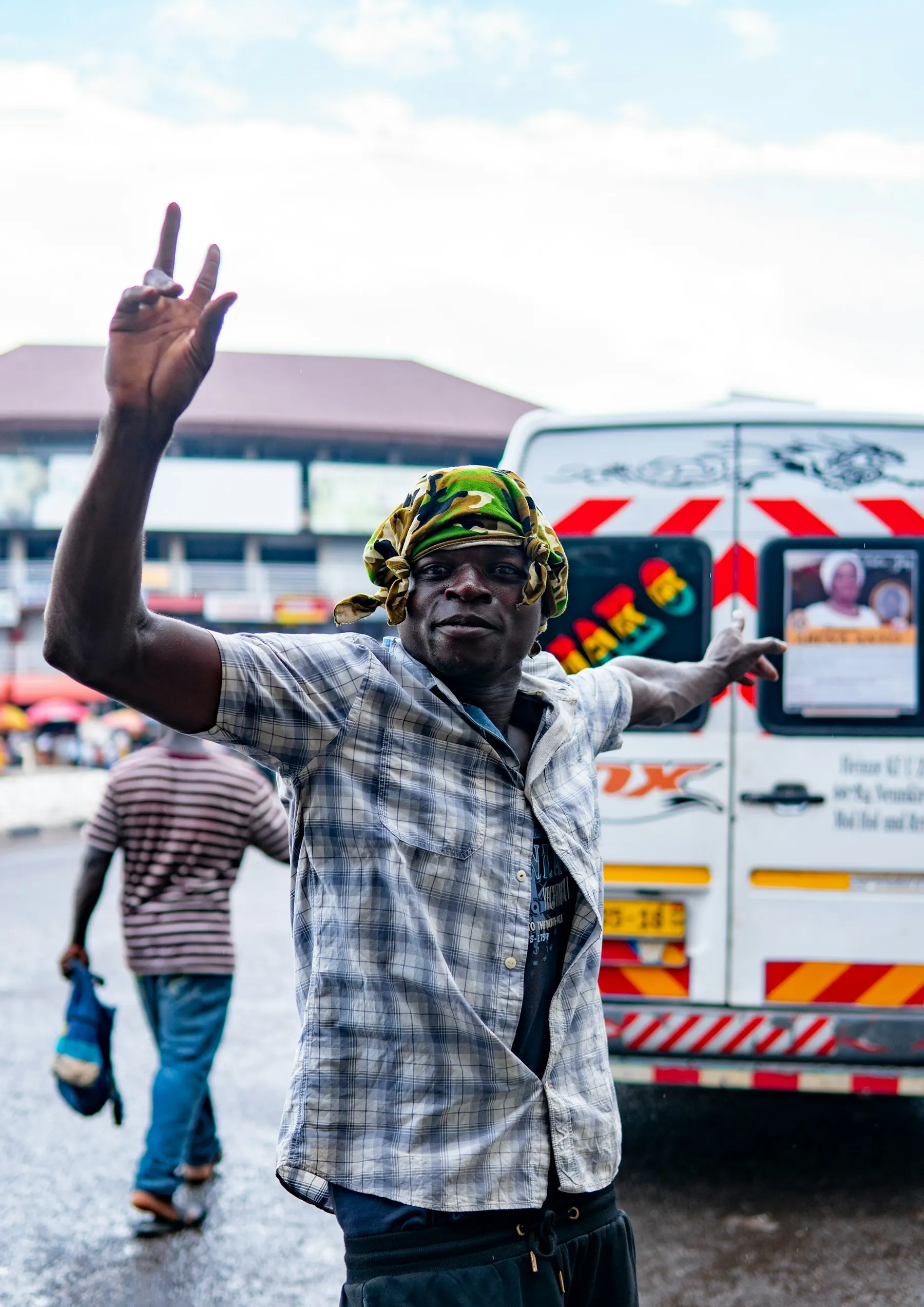 A man in a plaid shirt and yellow hard hat waving beside a bus